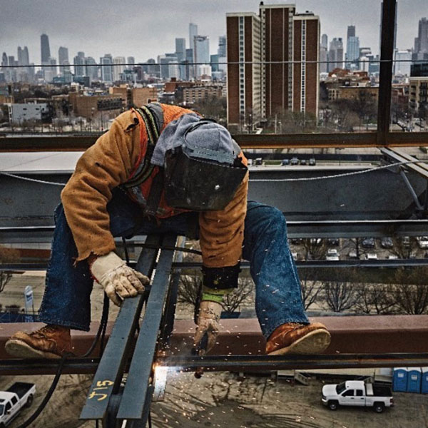 person welding iron to a beam on a construction site overlooking a city