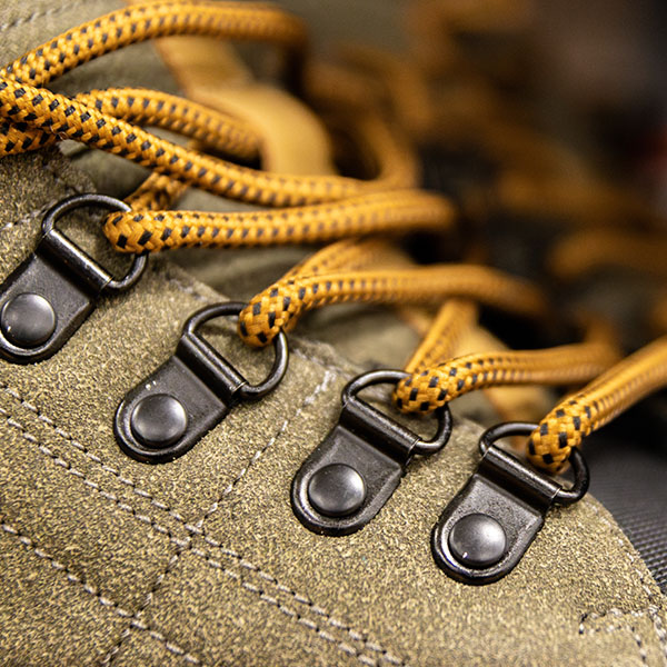 Close-up of olive green hiking boot with detailed focus on metal eyelets and bright yellow laces